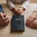 Manos de hombre, niño y anciana rodeando una Biblia negra con letras doradas sobre una mesa de madera clara.