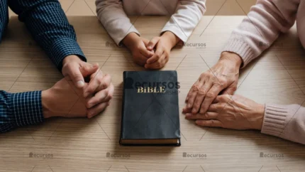 Primer plano cenital de manos de distintas edades descansando sobre madera junto a una Biblia en ambiente solemne.