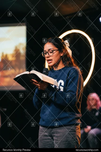 Joven mujer gafas moño blanco leyendo biblia abierta micrófono escenario oscuro aro luz circular cálida halo adoración contemporánea vertical desenfoque fondo