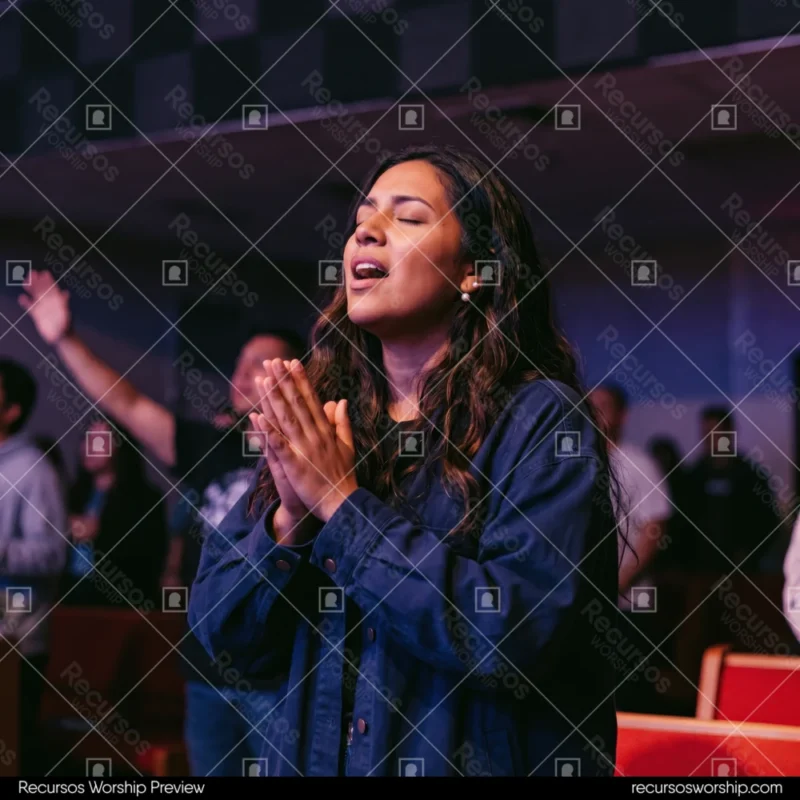 Mujer orando manos unidas ojos cerrados chaqueta denim mezclilla sillas rojas luces moradas congregacion adoracion culto cuadrado emotivo