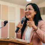 Mujer latina predicando blazer beige microfono atril madera biblia abierta escenario iglesia madera luces calidas horizontal profesional