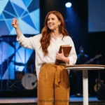 Mujer pelirroja biblia cerrada puno alzado luces led triangulos colores escenario culto fe valentia cuadrado luminoso
