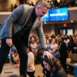 Pastor imponiendo manos mujer arrodillada oracion pantalla faith worship escenario culto sanidad intercesion vertical oscuro