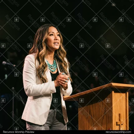 Mujer asiatica predicando podio acrilico microfono cruz madera fondo turquesa blazer escenario iglesia contemporanea cuadrado oscuro