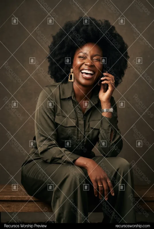 Mujer negra riendo afro mono verde oliva telefono pendientes dorados estudio fondo oscuro alegria vertical profesional