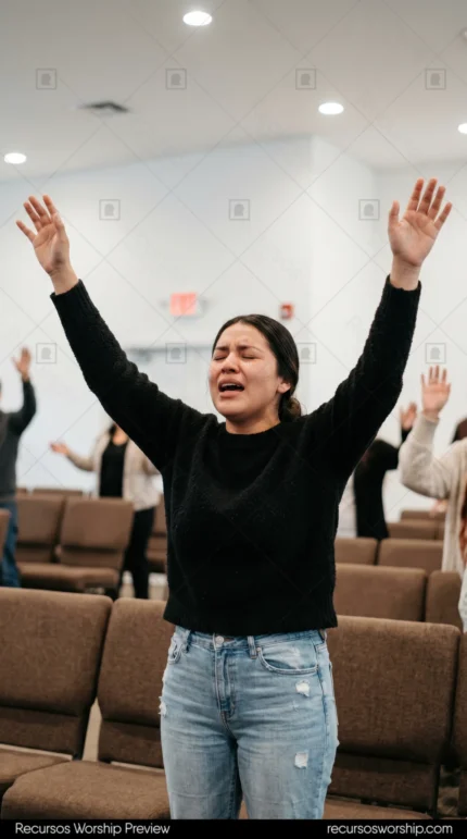 Mujer adoracion brazos alzados ojos cerrados sueter negro jeans sillas marrones congregacion iglesia vertical emotivo