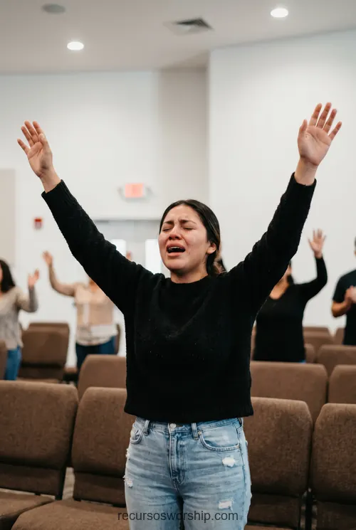 Mujer adoracion emocional brazos alzados ojos cerrados sueter negro jeans congregacion sillas marrones iglesia vertical