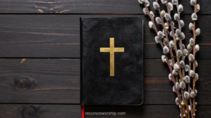 Biblia cerrada negra con cruz dorada grabada y marcapáginas rojo sobre tablones de madera oscura junto a ramas de sauce seco