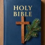 Holy Bible azul marino con letras doradas y cruz de madera natural junto a rama de pino verde sobre tablón de madera cálida