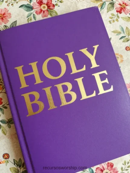 Biblia cerrada cubierta morada vibrante con letras doradas en relieve HOLY BIBLE sobre fondo floral rosado y verde suave