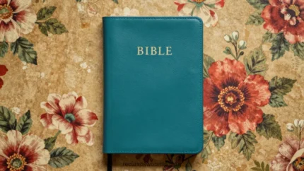 Biblia cerrada cubierta azul verdoso teal con inscripción dorada sobre papel tapiz vintage con flores rojas y hojas verdes cenital