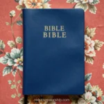 Biblia cerrada azul marino con letras doradas BIBLE sobre tela floral estampada en flores rosas y blancas vista cenital horizontal