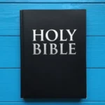 Holy Bible negra mate con letras blancas en relieve sobre tablones de madera pintada azul eléctrico brillante vista cenital