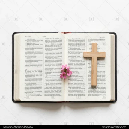 Biblia abierta en doble página con cruz de madera clara vertical y pequeño ramillete de flores rosas sobre fondo blanco cenital