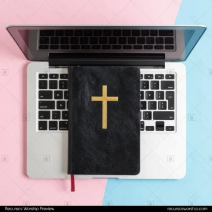 Biblia negra con cruz dorada sobre teclado de laptop plateado fondo bicolor rosa pastel y azul celeste vista cenital