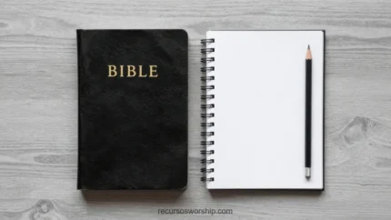 Biblia negra cerrada con letras doradas junto a cuaderno espiral abierto en blanco y lápiz negro sobre madera gris cenital