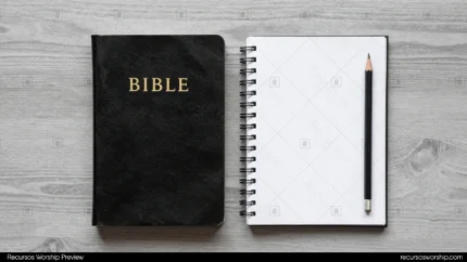 Biblia negra cerrada con letras doradas junto a cuaderno espiral abierto en blanco y lápiz negro sobre madera gris cenital