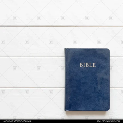 Biblia cerrada azul marino con letras doradas en esquina inferior derecha sobre tablones de madera blanca con espacio negativo cenital