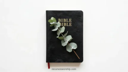 Biblia negra de cuero con letras doradas y marcapáginas rojo con rama de eucalipto verde grisáceo sobre fondo blanco vista cenital