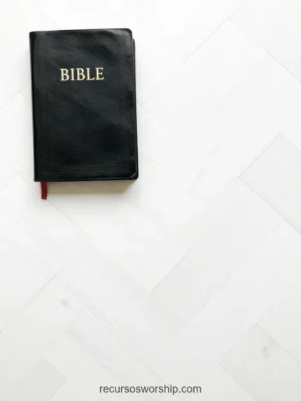 Biblia negra cerrada con letras doradas y marcapáginas rojo en esquina superior izquierda sobre parquet en espiga madera clara blanca cenital