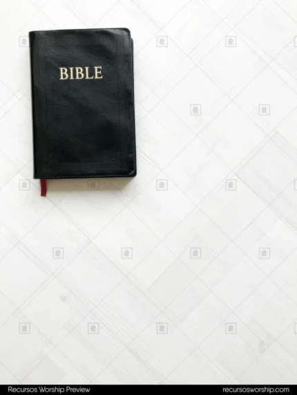 Biblia negra cerrada con letras doradas y marcapáginas rojo en esquina superior izquierda sobre parquet en espiga madera clara blanca cenital