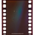 Fotograma pelicula analogica vacio perforaciones laterales marrones superficie oscura marron rojiza irisacion espectral azul verde cuadrado detalle vintage cinematografico celuloide