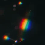 Destellos luz arcoiris dispersa haz central bokeh colorido fondo negro muy oscuro particulas luz difusa vertical prismatico atmosferico overlay