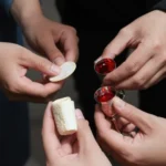 Varias manos adultas sosteniendo grupo oblea redonda blanca pan cortado copas pequenas vino rojo cenital intimo comunion comunitaria simultanea compartida colectiva santa cena