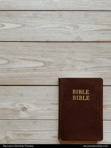 Biblia de cuero marrón rojizo con letras doradas en esquina inferior derecha sobre tablones de madera gris pintada con espacio negativo cenital
