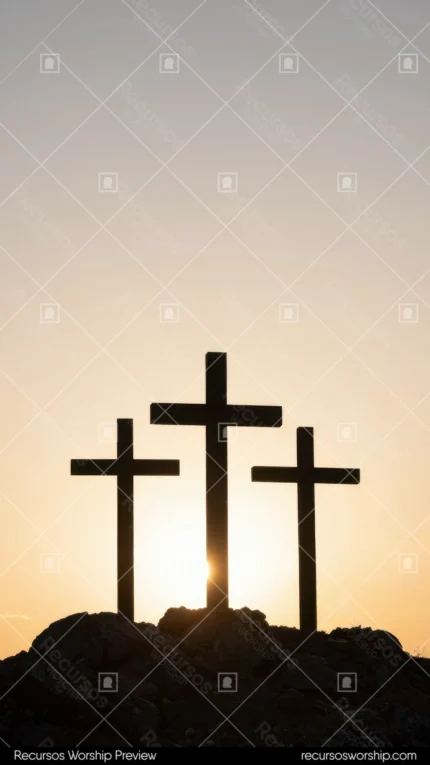 Tres cruces en silueta oscura sobre colina rocosa con sol detrás de la cruz central en cielo de atardecer dorado naranja pálido vertical