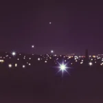 Paisaje nocturno urbano multiples destellos estelares luz artificial blanco amarillo fondo morado azul oscuro silueta edificios horizonte vertical cityscape bokeh starburst contemplativa mision ciudad