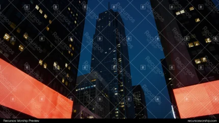 Vista bajo angulo canon urbano rascacielos cristal azul negro recortados cielo crepuscular paneles publicidad naranja rojo luminosos horizontal cinematografico oscuro city dark misional evangelismo ciudad