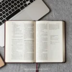 Escritorio con Biblia abierta al centro laptop gris cuaderno espiral marrón y taza de café sobre concreto gris texturizado vista cenital