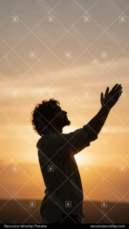 Silueta oscura de hombre de pie con brazos extendidos alzados en adoracion contra cielo atardecer dorado naranja horizonte amplio vertical