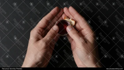 Manos adultas fondo negro profundo sosteniendo copa pequena cristal vino tinto pan pasas encima plano cenital intimo poderoso dramatico devocional santa cena oscuridad luz