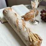 Baguette pan artesanal rustico espiga trigo primer plano biblia abierta copa plateada ornamentada vino racimo uvas fondo mesa madera calida vertical devocional rustico cotidiano santa cena