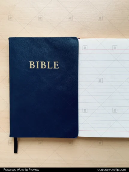 Biblia azul marino cerrada con letras doradas junto a cuaderno abierto de hojas rayadas en blanco sobre madera clara beige cenital