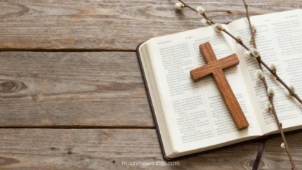 Biblia abierta en doble página con cruz de madera y ramas de sauce con amentos grises sobre tablones de madera rústica gris envejecida cenital
