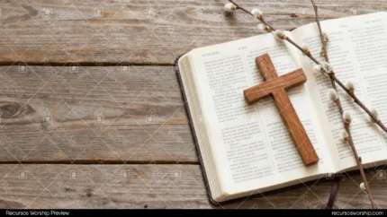 Biblia abierta en doble página con cruz de madera y ramas de sauce con amentos grises sobre tablones de madera rústica gris envejecida cenital