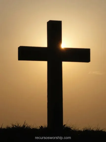 Silueta cruz madera negra grande colina hierba verde sol naranja dorado intenso horizonte halo luz cálida cielo degradado naranja amarillo vertical devocional clasico solemne viernes santo semana santa