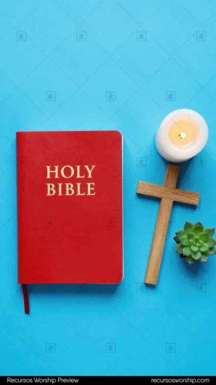 Holy Bible roja con letras doradas junto a cruz de madera vela blanca encendida y suculenta verde sobre fondo azul celeste brillante cenital vertical