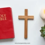 Holy Bible roja con letras doradas junto a cruz de madera natural vela blanca encendida y suculenta verde sobre fondo blanco liso cenital horizontal