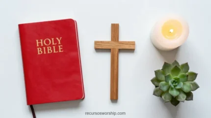 Holy Bible roja con letras doradas junto a cruz de madera natural vela blanca encendida y suculenta verde sobre fondo blanco liso cenital horizontal