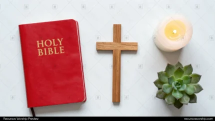 Holy Bible roja con letras doradas junto a cruz de madera natural vela blanca encendida y suculenta verde sobre fondo blanco liso cenital horizontal