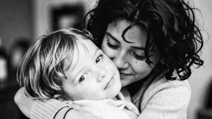 Retrato blanco negro madre cabello rizado abrazando hijo rubio pequeño primer plano intimo interior fondo difuso expresion ternura profunda horizontal